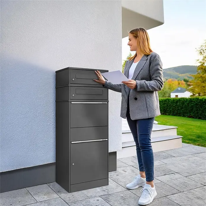 Metzler Paketbox 2 BRFK BISPO - L x B x H: 37,4 x 50,3 x 130,3 cm, Eisenglimmer, Stahl, Paketfach, 2 Briefkastenfächer - Moderner dunkelgrauer Mehrfach-Paketkasten an einem Haus, eine Frau legt Post hinein.