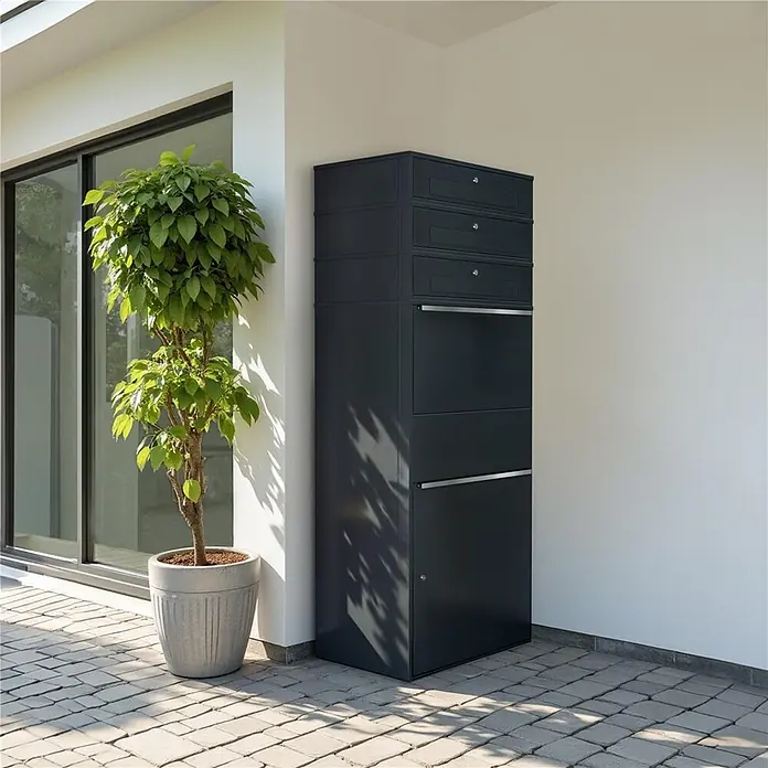 Metzler Paketbox XL 3 BRFK MAX - L x B x H: 45 x 72 x 177 cm, Anthrazit, Stahl, Paketfach, 3 Briefkastenfächer - Hoher dunkelgrauer Paketbriefkasten mit mehreren Fächern und silbernen Griffen, neben einem Haus.