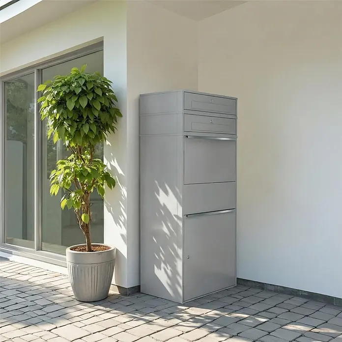 Metzler Paketbox XL 2 BRFK BISPO MAX - L x B x H: 45,4 x 72 x 161 cm, Graualuminium, Stahl, Paketfach, 2 Briefkastenfächer - Hoher grauer Paketkasten/Briefkasten mit mehreren Fächern neben einem Gebäude.