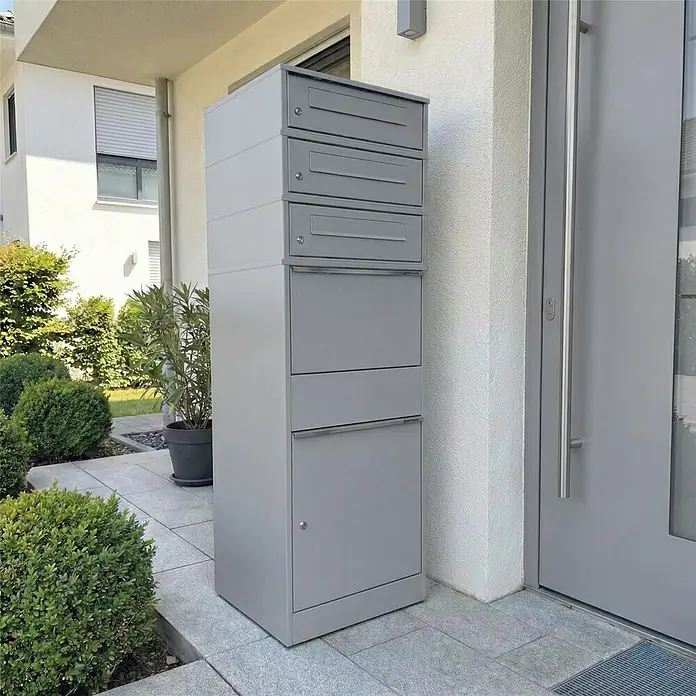 Metzler Paketbox 3 BRFK BISPO - L x B x H: 37,4 x 50,3 x 147,7 cm, Graualuminium, Stahl, Paketfach, 3 Briefkastenfächer - Graues Mehrfamilien-Briefkastensystem mit Paketbox vor einem modernen Hauseingang.