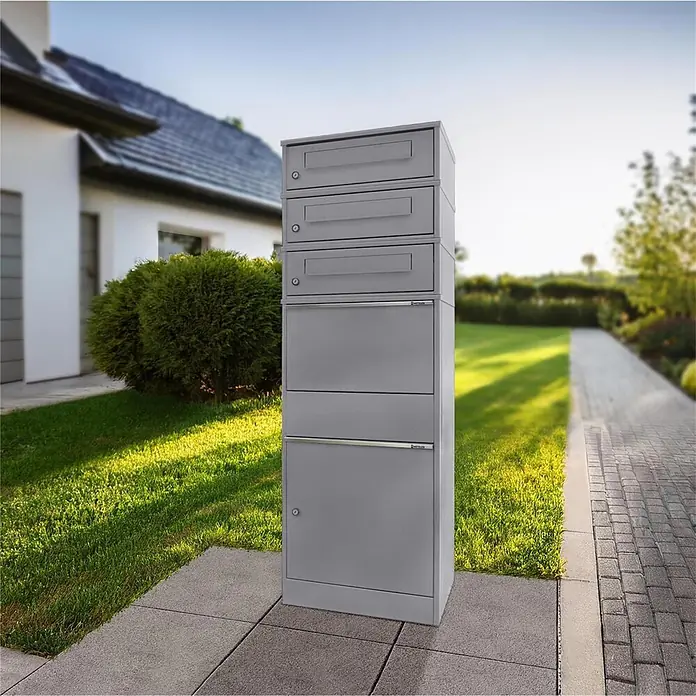 Metzler Paketbox 3 BRFK BISPO - L x B x H: 37,4 x 50,3 x 147,7 cm, Graualuminium, Stahl, Paketfach, 3 Briefkastenfächer - Hohes, graues modulares Briefkastensystem mit mehreren Fächern, auf gepflastertem Weg vor modernem Haus und Garten stehend.