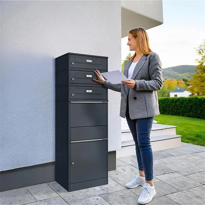 Metzler Paketbox 3 BRFK BISPO RE - L x B x H: 37,4 x 50,3 x 147,7 cm, Anthrazit, Stahl, Paketfach, 3 Briefkastenfächer und Namensschildern - Dunkelgraues Paketbriefkastensystem mit mehreren Fächern, das von einer Person zur Postzustellung genutzt wird.