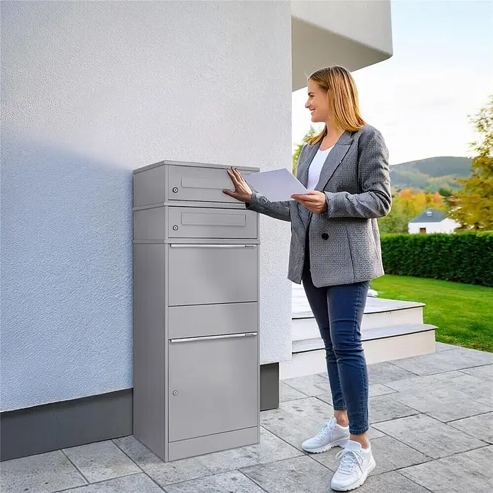 Metzler Paketbox 2 BRFK BISPO - L x B x H: 37,4 x 50,3 x 130,3 cm, Graualuminium, Stahl, Paketfach, 2 Briefkastenfächer - Hoher grauer Brief- und Paketkasten aus Metall für den Hausgebrauch. Eine Frau wirft Post in das oberste Fach.