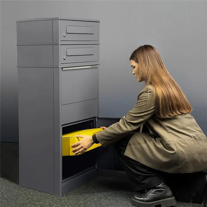 Metzler Paketbox 2 BRFK BISPO - L x B x H: 37,4 x 50,3 x 130,3 cm, Graualuminium, Stahl, Paketfach, 2 Briefkastenfächer - Dunkelgraue Paketbox mit mehreren Fächern. Eine Frau legt ein gelbes Paket in das unterste Fach.