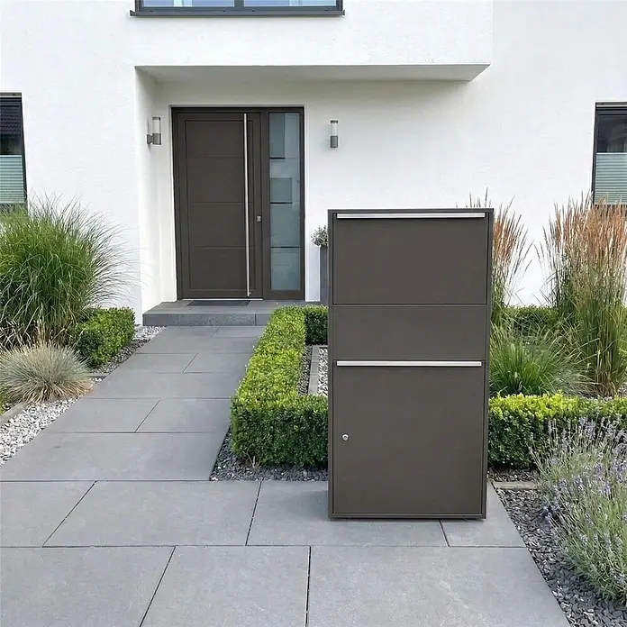 Metzler Paketbox XL BISPO MAX - L x B x H: 45,4 x 72 x 128,5 cm, Eisenglimmer, Stahl, Paketfach - Dunkelgrauer, moderner Paketbriefkasten mit silbernen Akzenten steht auf einem gepflasterten Weg neben dem Hauseingang, für Post- und Paketlieferungen.