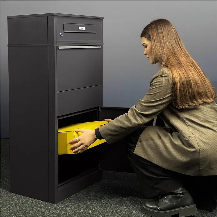 Metzler Paketbox BRFK BISPO RE - L x B x H: 37,4 x 50,3 x 112,9 cm, Eisenglimmer, Stahl, Paketfach - Dunkelgraue Paketbox mit integriertem Briefkasten. Eine Frau legt ein gelbes Paket in das untere Fach, was die Funktionalität zeigt.
