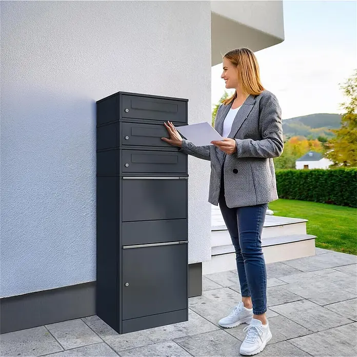 Metzler Paketbox 3 BRFK BISPO - L x B x H: 37,4 x 50,3 x 147,7 cm, Anthrazit, Stahl, Paketfach, 3 Briefkastenfächer - Dunkelgraues Paket- und Briefkastensystem mit mehreren Fächern an einem Haus, von einer Frau genutzt.