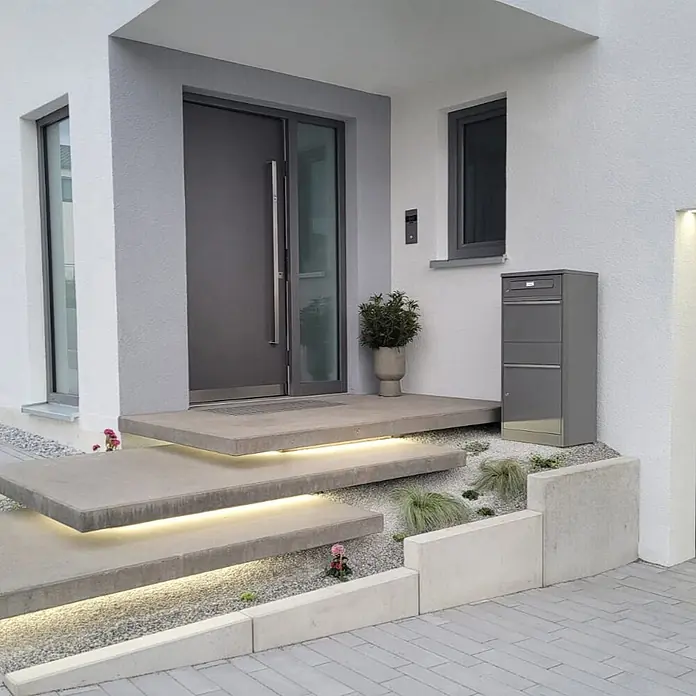 Metzler Paketbox BRFK BISPO RE - L x B x H: 37,4 x 50,3 x 112,9 cm, Graualuminium, Stahl, Paketfach - Moderner Hauseingang mit dunkelgrauer Tür, schwebenden Betonstufen mit LED-Beleuchtung und passendem grauem Paketkasten.