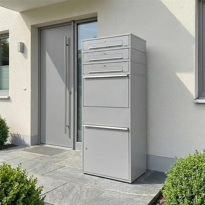 Metzler Paketbox XL 3 BRFK MAX - L x B x H: 45 x 72 x 177 cm, Graualuminium, Stahl, Paketfach, 3 Briefkastenfächer - Große graue Mehrfacheinwurf-Briefkasten- und Paketboxanlage neben einem Hauseingang.