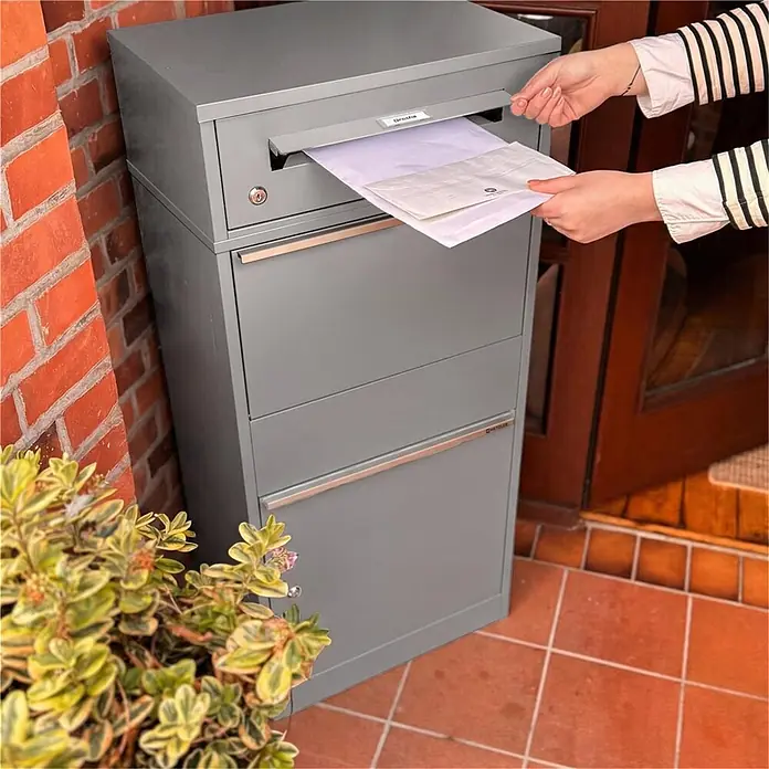 Metzler Paketbox BRFK BISPO RE - L x B x H: 37,4 x 50,3 x 112,9 cm, Graualuminium, Stahl, Paketfach - Großer grauer Paketbriefkasten aus Metall, in den eine Person Post einwirft.
