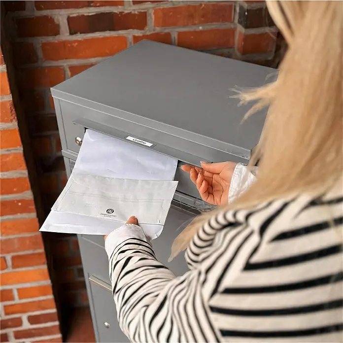 Metzler Paketbox BRFK BISPO RE - L x B x H: 37,4 x 50,3 x 112,9 cm, Graualuminium, Stahl, Paketfach - Grauer Briefkasten mit 'Grothe' Beschriftung. Eine Person legt weiße Umschläge in den Schlitz.