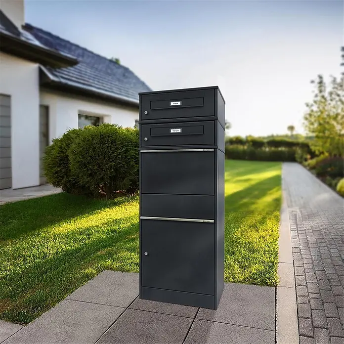 Metzler Paketbox 2 BRFK BISPO RE - L x B x H: 37,4 x 50,3 x 130,3 cm, Anthrazit, Stahl, Namensschild, Mit 2 Briefkastenfächern und Namensschildern - Dunkelgrauer Mehrfach-Briefkastenständer vor einem modernen Haus, harmonisch in die Umgebung integriert.