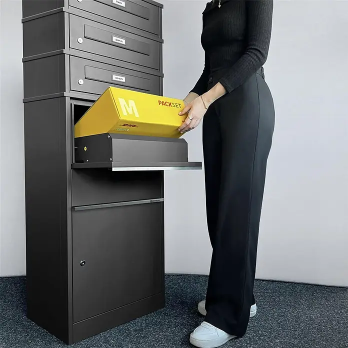 Metzler Paketbox 3 BRFK BISPO RE - L x B x H: 37,4 x 50,3 x 147,7 cm, Eisenglimmer, Stahl, Namensschild, 3 Briefkastenfächer und Namensschildern - Dunkelgraue Mehrfach-Paketbox, eine Person legt ein gelbes Paket in den großen Einwurfschlitz.