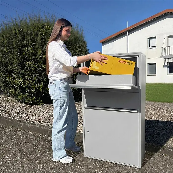 Metzler Paketbox XL BISPO MAX - L x B x H: 45,4 x 72 x 128,5 cm, Graualuminium, Stahl, Paketfach - Eine Person legt ein gelbes Paket in eine graue Metall-Paketbox.