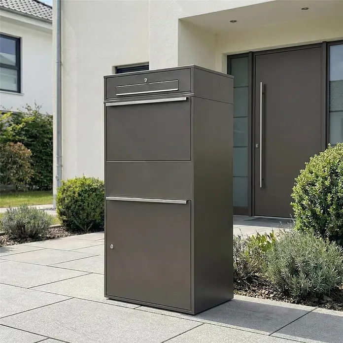 Metzler Paketbox XL BRFK BISPO MAX - L x B x H: 45,4 x 72 x 145 cm, Eisenglimmer, Stahl, Paketfach - Dunkelgrauer Metall-Paketbriefkasten im modernen Design, auf einem gepflasterten Weg vor einem Haus stehend.