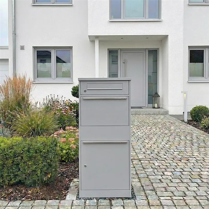 Metzler Paketbox BRFK BISPO - L x B x H: 37,4 x 50,3 x 112,9 cm, Graualuminium, Stahl, Paketfach - Graue Paket- und Briefkastenanlage aus Metall, freistehend vor einem modernen Haus.