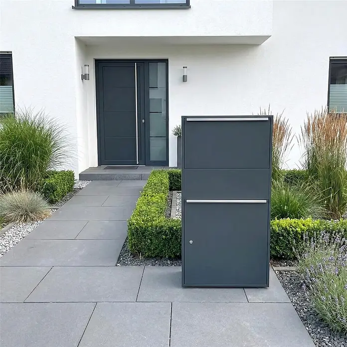 Metzler Paketbox XL BISPO MAX - L x B x H: 45,4 x 72 x 128,5 cm, Anthrazit, Stahl, Paketfach - Dunkelgrauer Paket- und Briefkasten auf einem gepflasterten Weg vor einem modernen Hauseingang.