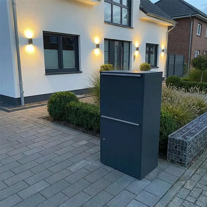 Metzler Paketbox XL BISPO MAX - L x B x H: 45,4 x 72 x 128,5 cm, Anthrazit, Stahl, Paketfach - Ein freistehender dunkelgrauer Paketbriefkasten mit mehreren Fächern, auf einer gepflasterten Auffahrt neben einem modernen Hauseingang platziert.