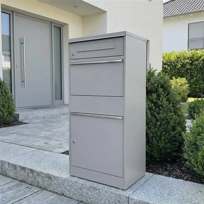 Metzler Paketbox BRFK BISPO - L x B x H: 37,4 x 50,3 x 112,9 cm, Graualuminium, Stahl, Paketfach - Hoher grauer Paketbriefkasten aus Metall mit Briefschlitz und zwei Fächern, neben einem modernen Hauseingang.