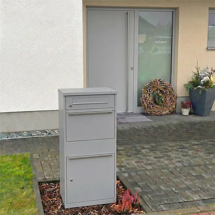 Metzler Paketbox BRFK BISPO - L x B x H: 37,4 x 50,3 x 112,9 cm, Graualuminium, Stahl, Paketfach - Hoher grauer Brief- und Paketkasten aus Metall vor einem modernen Hauseingang.
