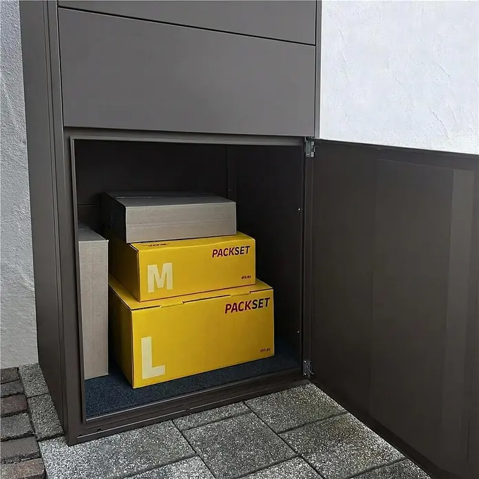 Metzler Paketbox XL BRFK MAX RE - L x B x H: 45,4 x 72 x 145 cm, Eisenglimmer, Stahl, Paketfach - Dunkelbraune Paketbox mit offener Tür, die mehrere Pakete, darunter gelbe DHL PACKSET Kartons, enthält.