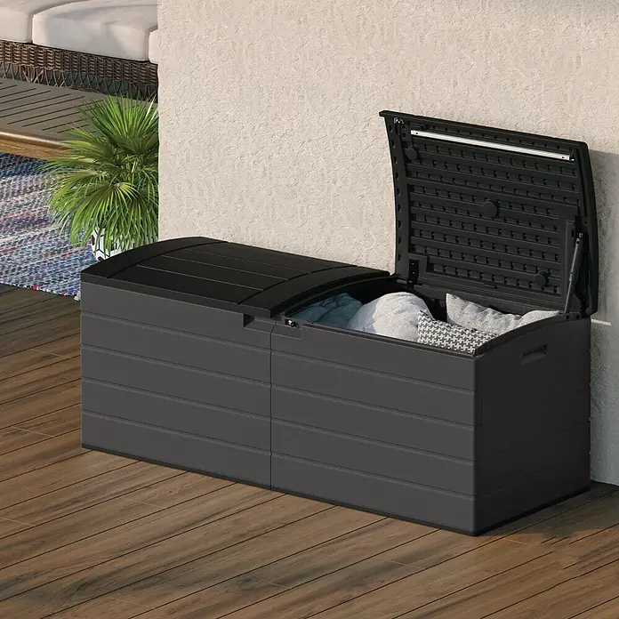 Suncast Auflagenbox - 150 x 61 x 64 cm, Kunststoff, Anthrazit, Geteilter Deckel - Dunkelgraue Outdoor-Aufbewahrungsbox mit geöffnetem Deckel, gefüllt mit Kissen, auf einer Holzterrasse an einer Wand.