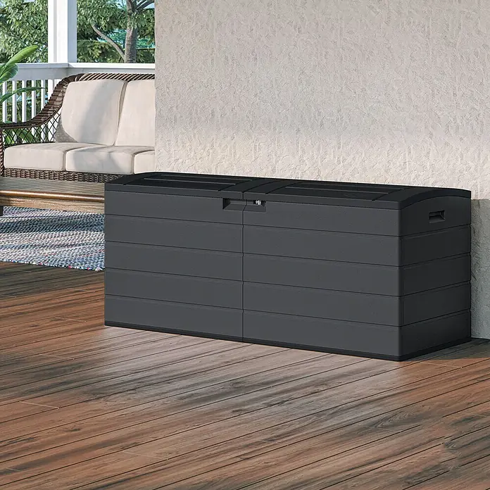 Suncast Auflagenbox - 150 x 61 x 64 cm, Kunststoff, Anthrazit, Geteilter Deckel - Dunkelgraue Kunststoff-Outdoor-Aufbewahrungsbox auf Holzterrasse neben einer strukturierten Wand. Bietet viel Stauraum im Freien.
