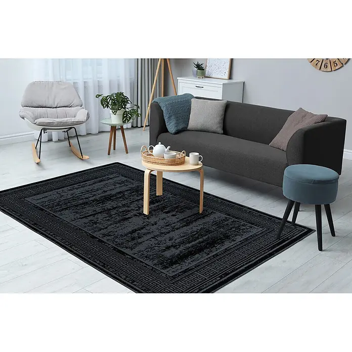 Kayoom Flachgewebeteppich Kalea 325 - Schwarz, 170 x 120 cm, 100 % Polyester - Großer schwarzer Teppich mit abstraktem Muster und geometrischem Rand, im Wohnzimmer platziert.