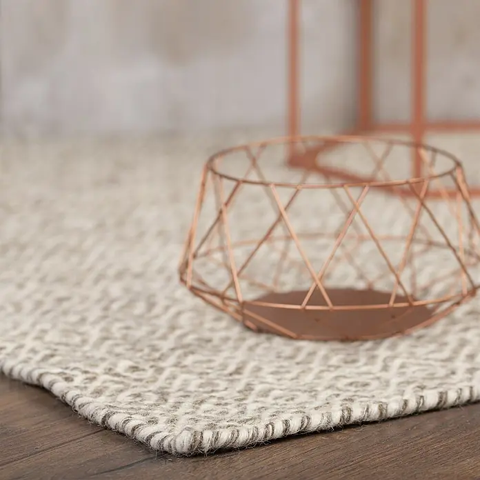 Kayoom Wollteppich Bombay 344 - Taupe, 230 x 160 cm, 100 % Wolle - Ein geometrischer, kupferfarbener Drahtkorb liegt auf einem strukturierten hellen Teppich und betont eine moderne Ästhetik.
