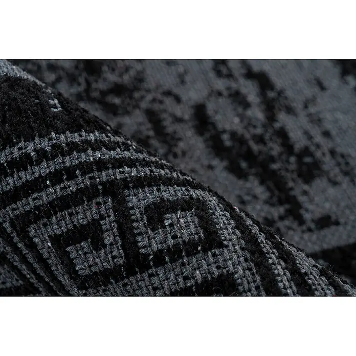 Kayoom Flachgewebeteppich Kalea 325 - Schwarz, 170 x 120 cm, 100 % Polyester - Nahaufnahme eines dunkelgrau-schwarzen gemusterten Teppichs, der seine gewebte Textur beim Falten zeigt.