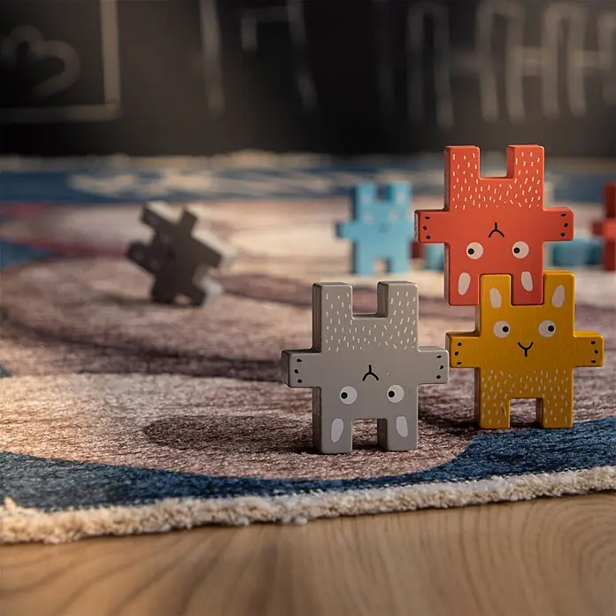 Kayoom Kinderteppich Joanna 623 - Multi, 170 x 115 cm, 70 % Baumwolle, 30 % Polyester - Bunte Holz-Tierpuzzle-Teile, darunter gestapelte graue, gelbe und rote Hasen, auf einem gemusterten Teppich.