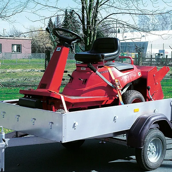 Conacord Spanngurt - 8 m x 5 cm, Belastbarkeit: 2.000 kg, Einteilig, Mit Ratsche - Roter Rasentraktor auf einem Anhänger mit silbernen Seitenwänden und einem schwarzen Kotflügel, der im Freien steht.