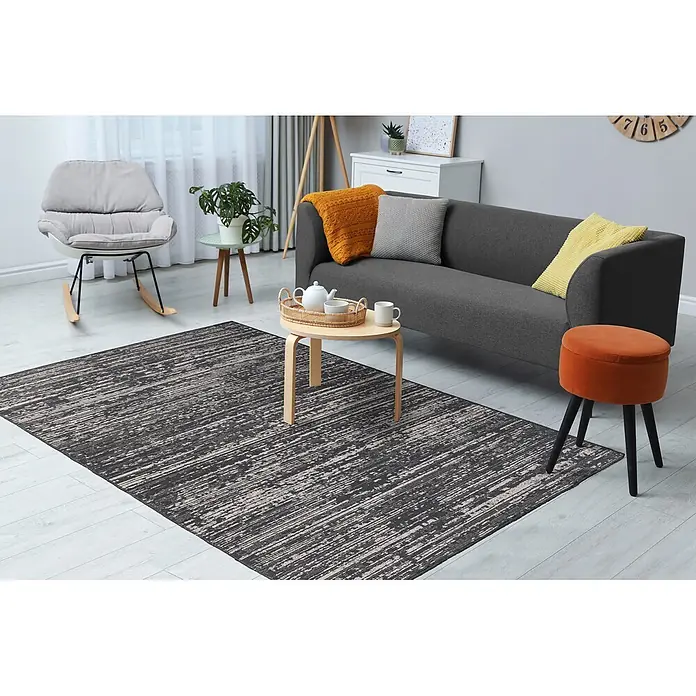 Kayoom Flachgewebeteppich Kalea 125 - Grau, 170 x 120 cm, 100 % Polyester - Ein rechteckiger dunkelgrauer Teppich mit zerrissenen hellgrauen Querstreifen bedeckt einen hellen Holzfußboden in einem gemütlichen Wohnzimmer.