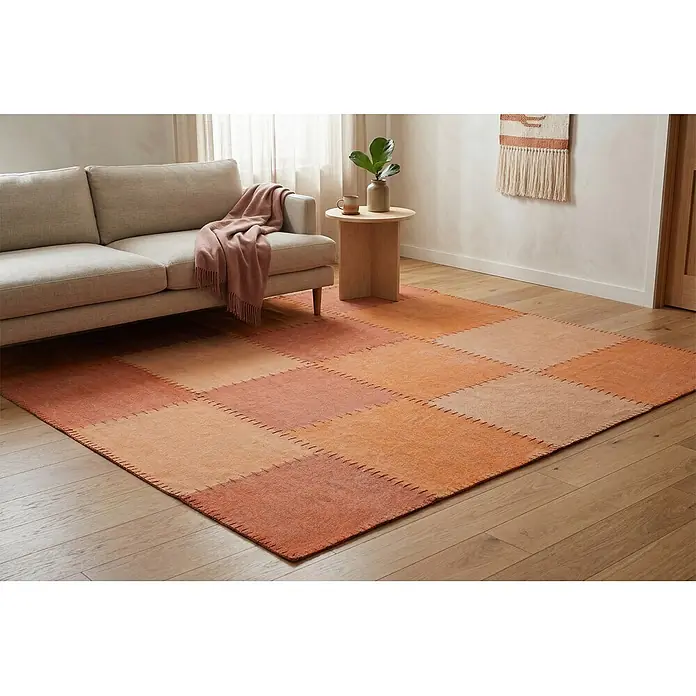 Kayoom Flachgewebeteppich Lyrical 110 - Multi/Orange, 230 x 160 cm, 100 % Baumwolle - Ein großer rechteckiger Patchwork-Teppich in Orange- und Terrakottatönen auf Holzfußboden unter einem hellen Sofa.