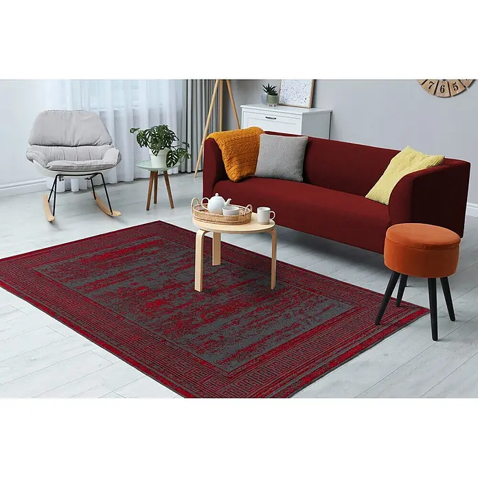 Kayoom Flachgewebeteppich Kalea 325 - Rot, 150 x 80 cm, 100 % Polyester - Rot-dunkelgrauer Teppich mit geometrischer Bordüre, auf hellem Holzboden in einem Wohnzimmer unter einem Couchtisch.