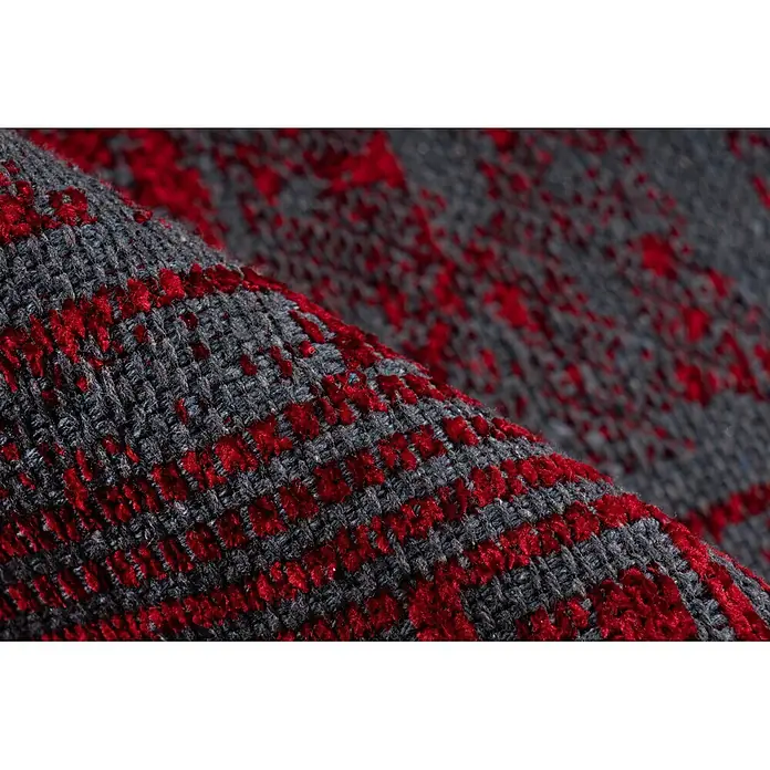 Kayoom Flachgewebeteppich Kalea 325 - Rot, 150 x 80 cm, 100 % Polyester - Nahaufnahme von strukturiertem dunkelgrauem Stoff mit leuchtend roten Mustern, der seinen weichen Flor zeigt.