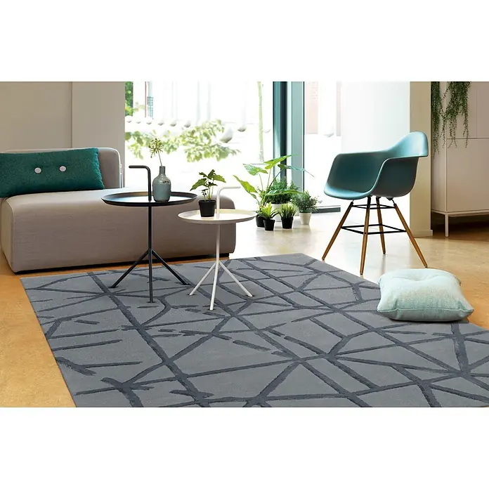 Kayoom Kurzflorteppich Satin 8063 - Grau, 180 x 120 cm, 70 % Wolle, 30 % Viskose - Grauer Teppich mit dunklem geometrischem Muster, in einem modernen Wohnzimmer unter Möbeln platziert.