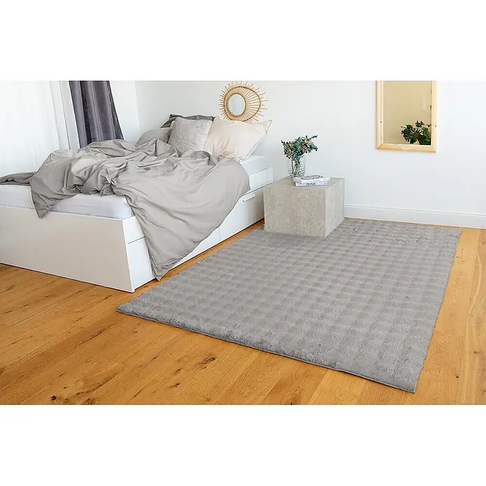Kayoom Fellteppich Hailey 125 - Grau, 120 x 160 cm, 100 % Polyester - Ein rechteckiger, flauschiger grauer Teppich mit Strukturmuster, auf Holzboden in einem Schlafzimmer platziert.