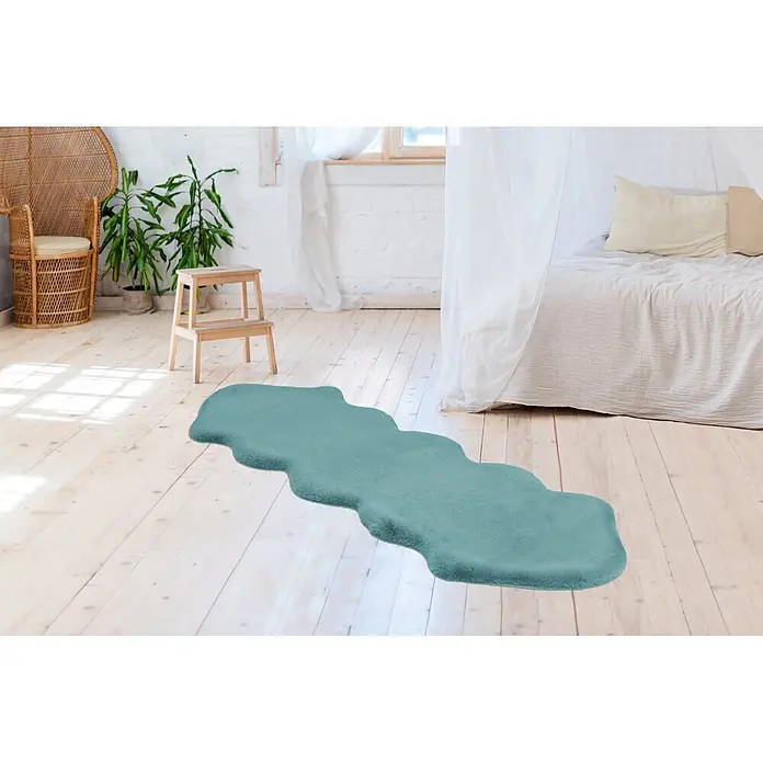 Kayoom Kunstfell Rabbit Double Sheepskin - Türkis, 180 x 60 cm, 100 % Polyester - Ein wellenförmiger, türkisfarbener Teppich auf hellem Holzboden in einem Schlafzimmer.