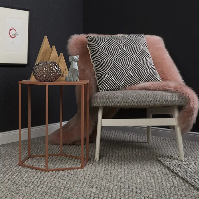 Kayoom Wollteppich Attic 590 - Silber, 170 x 120 cm, 50 % Wolle, 50 % Viskose - Eine gemütliche Ecke mit grauem Polsterstuhl, rosa Kunstfellwurf und geometrischem Kissen. Ein rostfarbener sechseckiger Beistelltisch trägt Dekoartikel.