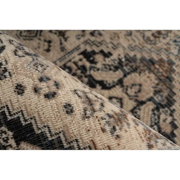 Kayoom Kurzflorteppich Charin 425 - Blau, 230 x 160 cm, 100 % Polypropylen - Nahaufnahme eines gerollten beigefarbenen Teppichs mit dunkelblauen, braunen und hellblauen geometrischen Mustern, der seine weiche Florstruktur zeigt.