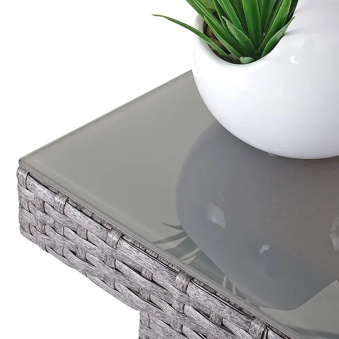 Mendler Gartenmöbel-Set - 7 -tlg., Polyrattan, Grau, Kissen creme, Grau, Kissen creme - Ecke eines grauen Rattan-Tisches mit Glasplatte, darauf ein weißer Topf mit einer Grünpflanze.