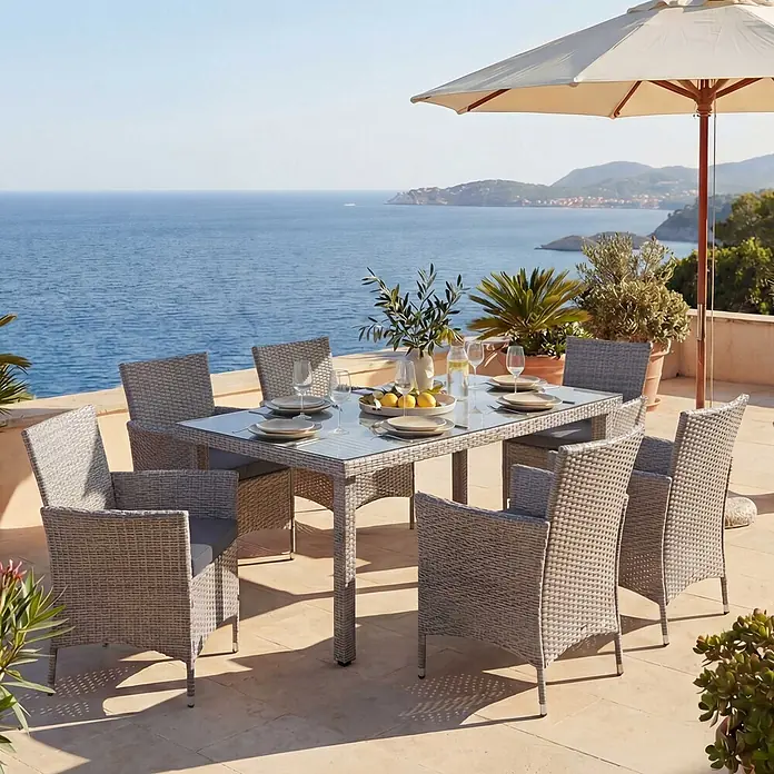 Mendler Gartenmöbel-Set - 7 -tlg., Polyrattan, Grau, Kissen anthrazit, Grau, Kissen anthrazit - Graues Rattan-Gartenset mit Glastisch und sechs Stühlen auf einer Terrasse mit Meerblick, gedeckt für eine Mahlzeit.