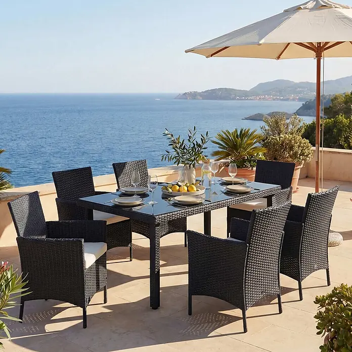 Mendler Poly-Rattan-Garnitur Halden - anthrazit, Kissen Creme -  - Schwarzes Outdoor-Esszimmer-Set im Rattan-Stil mit Glastisch und Stühlen, auf einer Terrasse am Meer gedeckt.