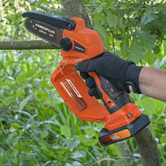 PowerPlus Tijeras para podar de batería + Motosierra - 20 V, 1 batería, 2 Ah, Grosor de rama máx.: 30 mm - Miniserra de cadena inalámbrica POWERPLUS naranja y negra podando una rama. Una mano enguantada sostiene la herramienta.
