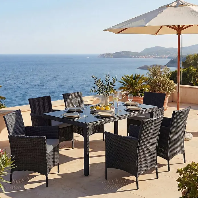 Mendler Poly-Rattan-Garnitur Halden - anthrazit, Kissen anthrazit -  - Schwarze Outdoor-Essgruppe aus Polyrattan mit Glasplatte und grauen Kissen, auf einer Terrasse mit Meerblick.