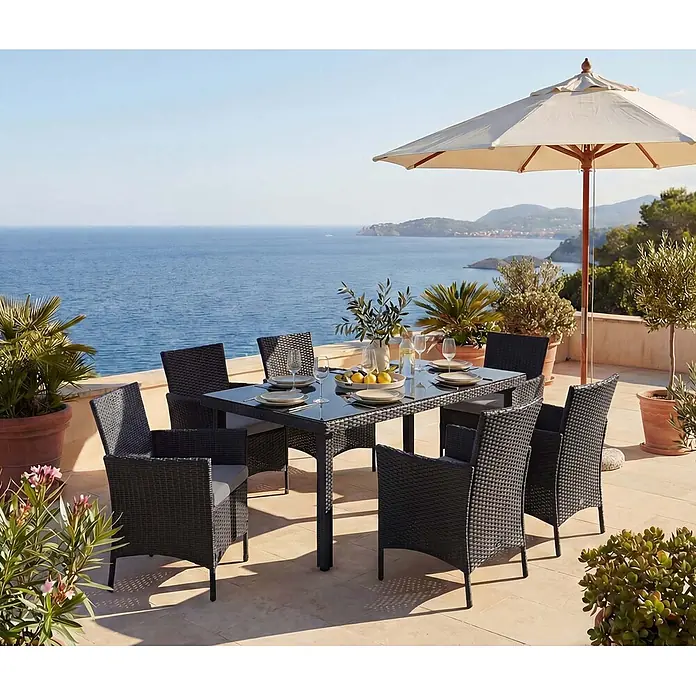 Mendler Poly-Rattan-Garnitur Halden - anthrazit, Kissen anthrazit -  - Schwarzes Korbmöbel-Gartenset mit Glastisch und Stühlen, auf einer sonnigen Terrasse mit Meerblick.