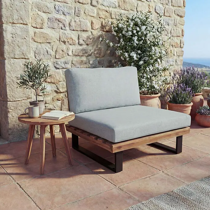 Mendler Garten-Loungesessel HWC-H54 - 1 Stk., Holz, Hellbraun, Polster hellgrau, B x T x H: 82 x 82 x 75 cm - Outdoor-Loungesessel mit hellgrauen Kissen, Holzrahmen und dunklen Metallbeinen, neben einem kleinen Holztisch auf einer Terrasse.