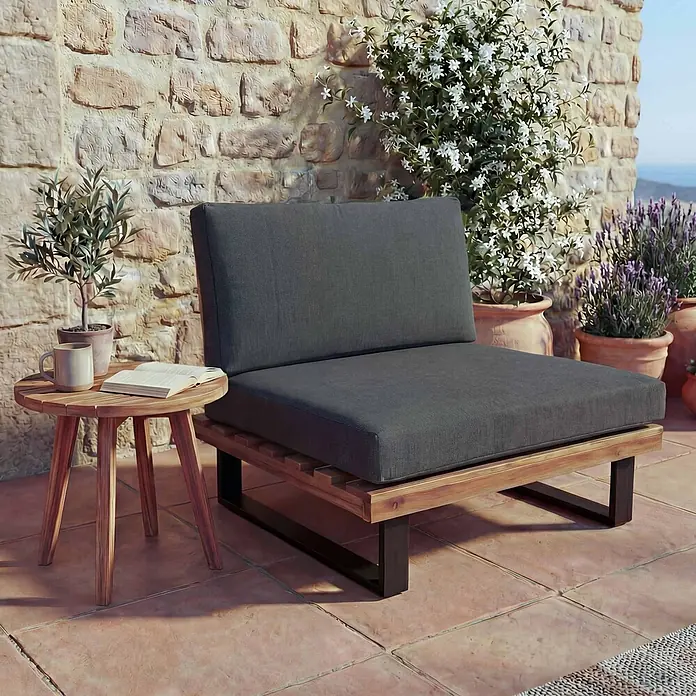 Mendler Garten-Loungesessel HWC-H54 - 1 Stk., Holz, Braun, Polster dunkelgrau, B x T x H: 82 x 82 x 75 cm - Outdoor-Loungesessel mit dunkelgrauen Kissen und Holzrahmen mit schwarzen Beinen, daneben ein Beistelltisch aus Holz auf einer Terrasse.