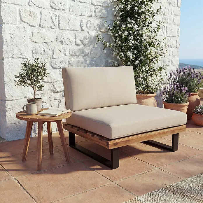 Mendler Garten-Loungesessel HWC-H54 - 1 Stk., Holz, Hellbraun, Polster beige, B x T x H: 82 x 82 x 75 cm - Gartenliegestuhl mit beigen Kissen, Holzrahmen und schwarzen Metallbeinen, neben einem runden Holztisch auf einer Terrasse.